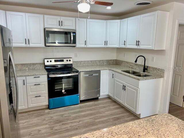 kitchen with white cabinets, sink, stainless steel appliances, and light hardwood / wood-style flooring