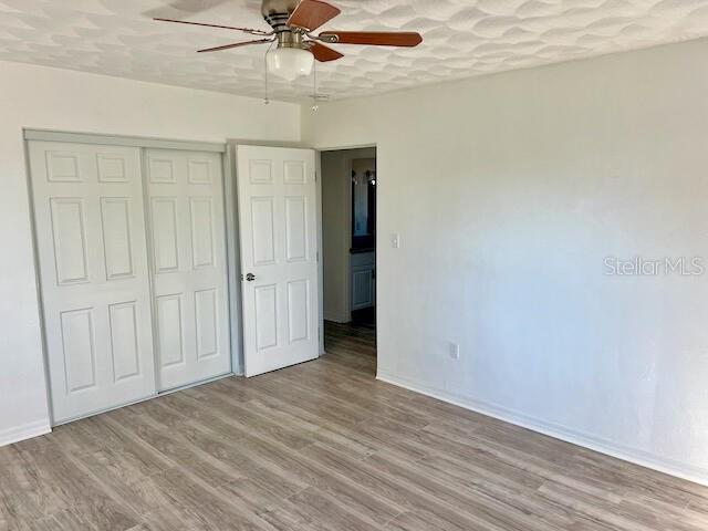 unfurnished bedroom featuring ceiling fan, a closet, a textured ceiling, and light wood-type flooring