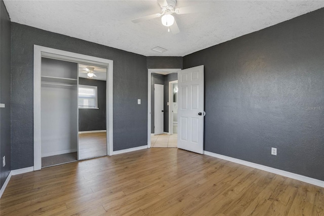 unfurnished bedroom with light wood-type flooring, a textured ceiling, ceiling fan, and a closet