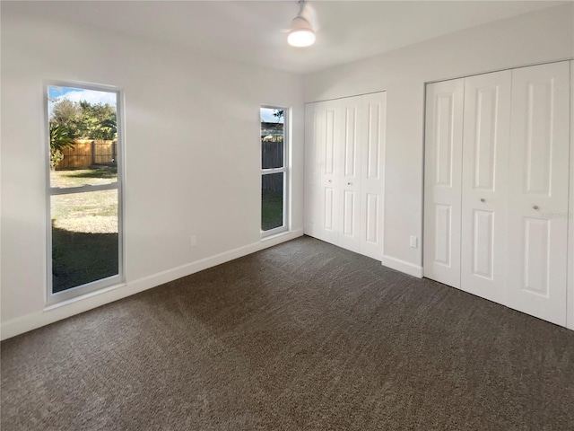 unfurnished bedroom with two closets and dark colored carpet