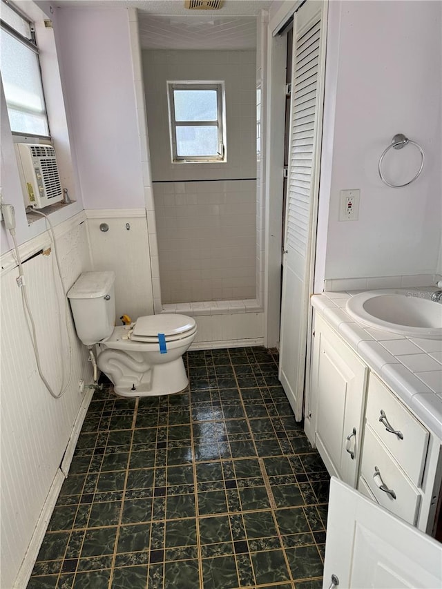 bathroom with a tile shower, vanity, toilet, and cooling unit