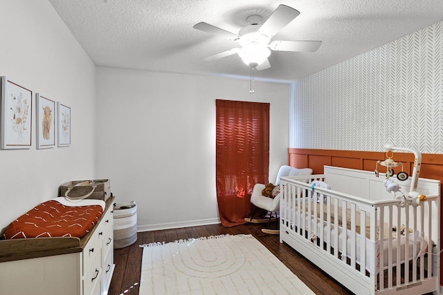 bedroom with a crib, a textured ceiling, ceiling fan, and dark wood-type flooring