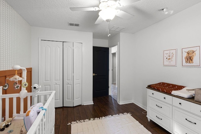 bedroom with a textured ceiling, ceiling fan, dark wood-type flooring, and a closet