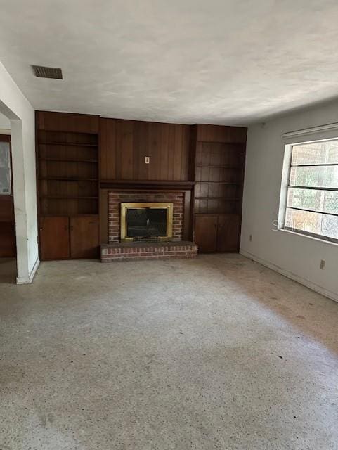 unfurnished living room featuring wood walls and a brick fireplace