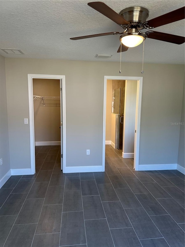 unfurnished bedroom with ceiling fan, a walk in closet, a closet, and a textured ceiling