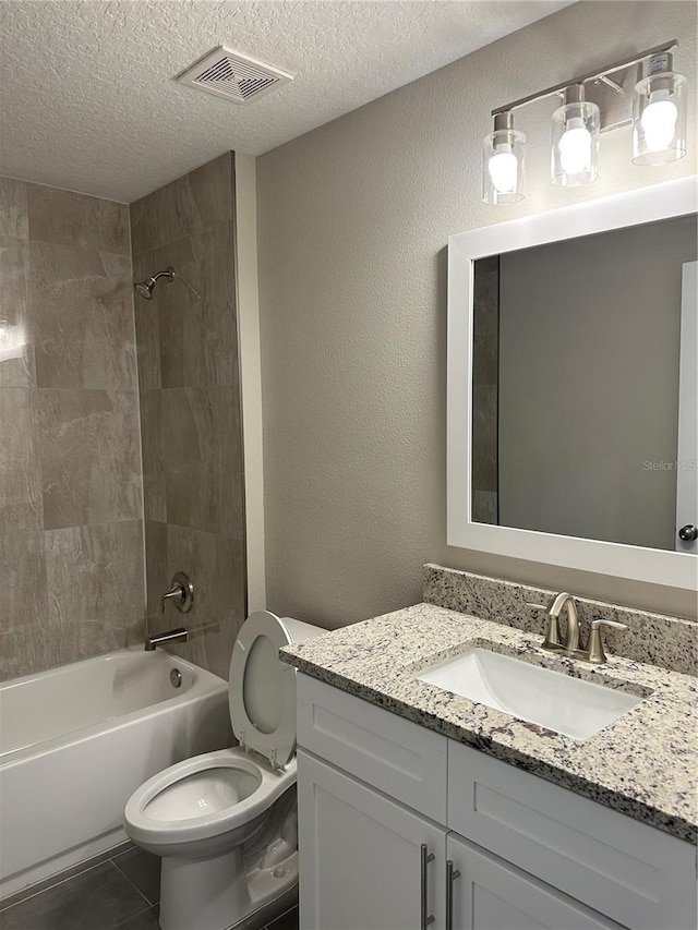 full bathroom with tiled shower / bath, tile patterned flooring, vanity, toilet, and a textured ceiling