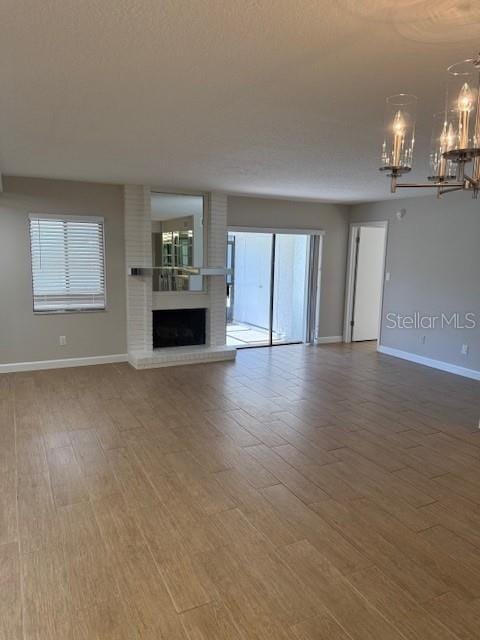 unfurnished living room featuring hardwood / wood-style floors, a notable chandelier, and a brick fireplace