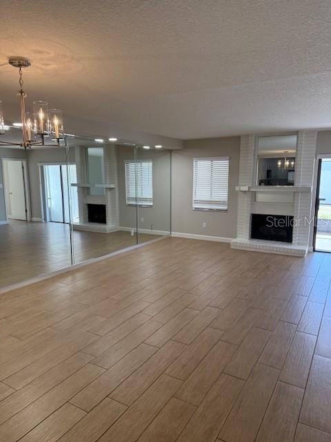 unfurnished living room featuring plenty of natural light, an inviting chandelier, and a brick fireplace