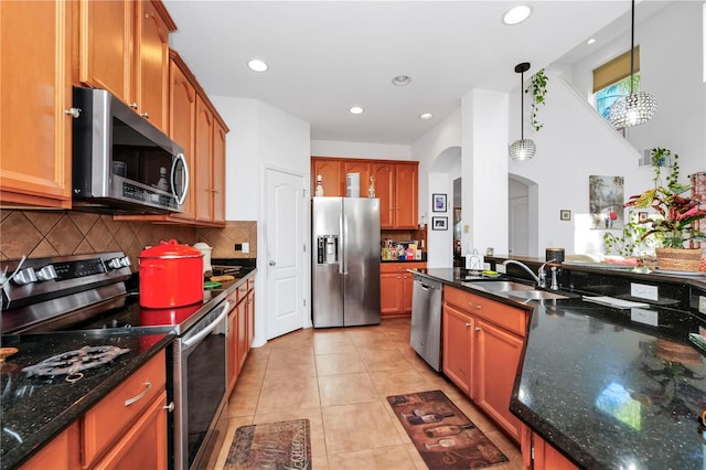 kitchen featuring appliances with stainless steel finishes, sink, light tile patterned floors, decorative light fixtures, and dark stone countertops