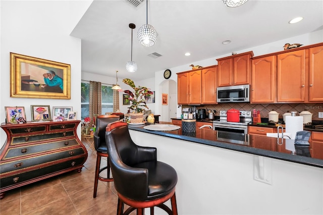 kitchen featuring backsplash, a breakfast bar, stainless steel appliances, decorative light fixtures, and tile patterned flooring