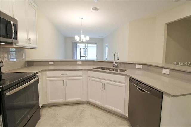 kitchen with kitchen peninsula, appliances with stainless steel finishes, sink, a notable chandelier, and white cabinets