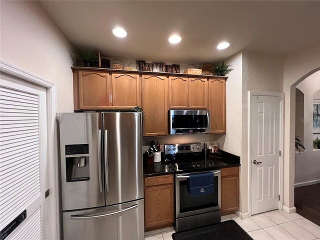 kitchen with light tile patterned floors, stainless steel appliances, and dark stone counters