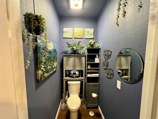 bathroom with toilet, wood finished floors, and a textured wall