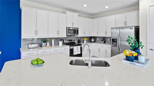 kitchen with white cabinets, appliances with stainless steel finishes, light stone counters, and sink