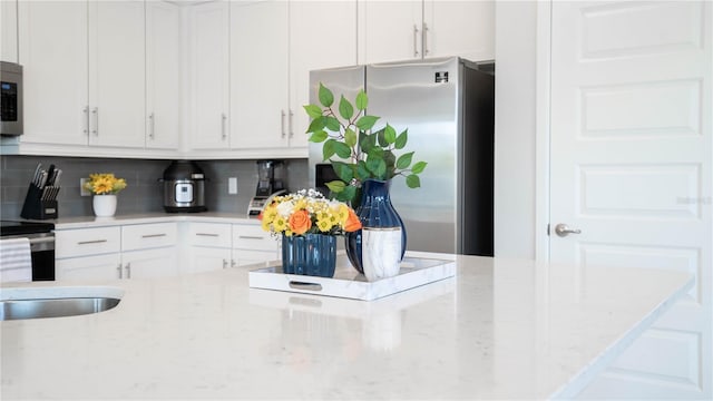 kitchen with white cabinetry, sink, stainless steel appliances, light stone counters, and decorative backsplash