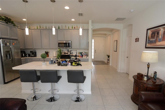 kitchen featuring a kitchen breakfast bar, stainless steel appliances, gray cabinets, a kitchen island, and hanging light fixtures