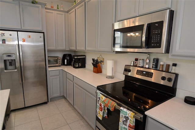 kitchen with light stone countertops, light tile patterned floors, stainless steel appliances, and gray cabinets