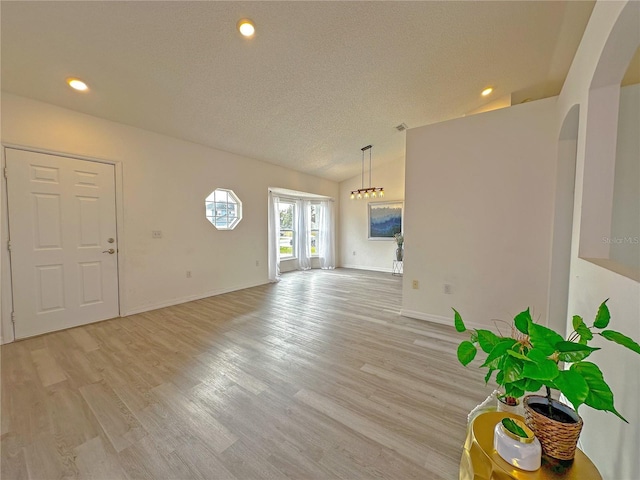 unfurnished living room featuring a textured ceiling, light hardwood / wood-style flooring, and vaulted ceiling