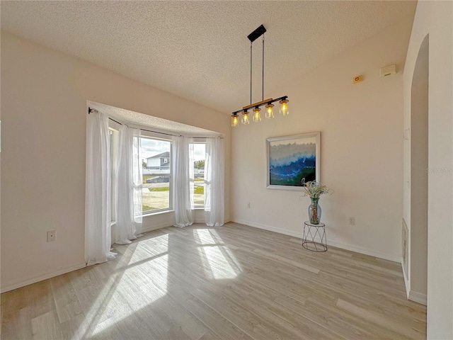 unfurnished dining area with a textured ceiling and light wood-type flooring