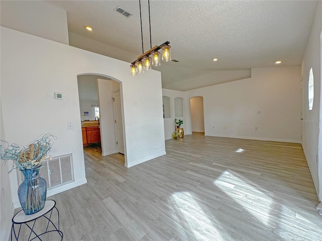 unfurnished dining area featuring light wood-type flooring, a textured ceiling, and vaulted ceiling