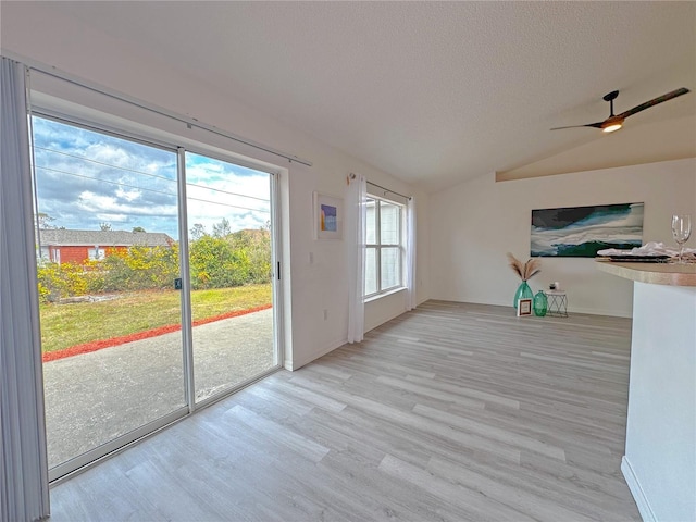 unfurnished living room featuring a textured ceiling, ceiling fan, light hardwood / wood-style flooring, and vaulted ceiling