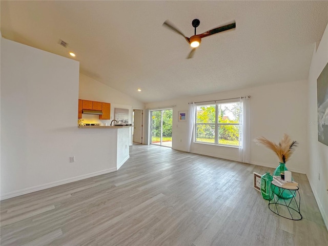 unfurnished living room with a textured ceiling, ceiling fan, light hardwood / wood-style flooring, and vaulted ceiling