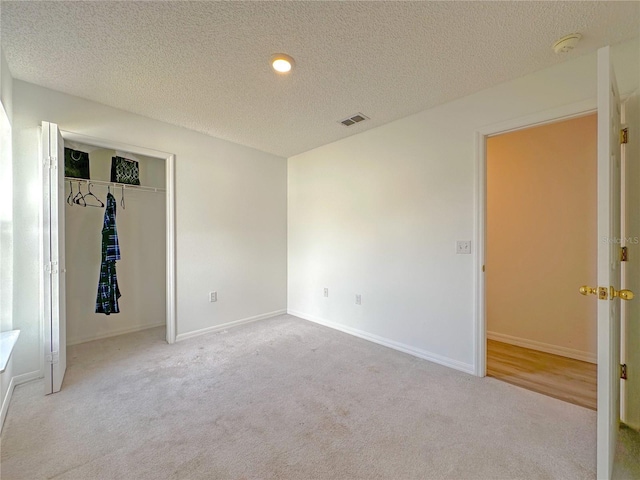 unfurnished bedroom with a textured ceiling, light carpet, and a closet