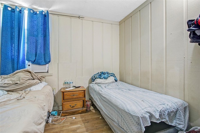 bedroom with cooling unit, wood-type flooring, a textured ceiling, and wooden walls