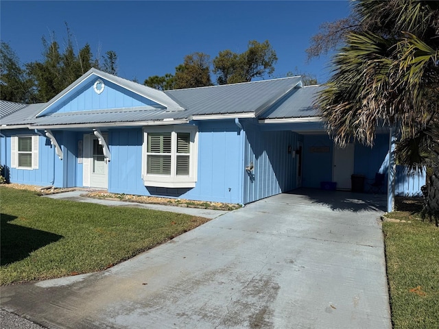 ranch-style house with board and batten siding, a front yard, metal roof, a carport, and driveway