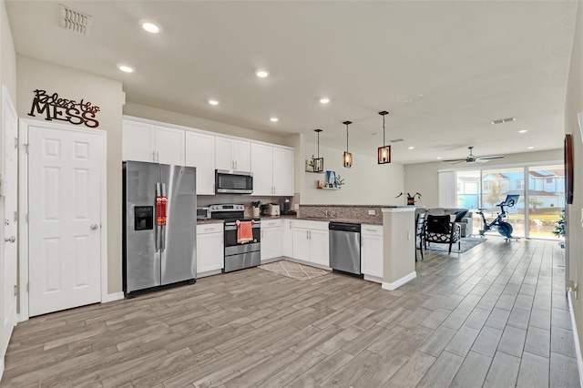 kitchen featuring appliances with stainless steel finishes, pendant lighting, white cabinetry, light hardwood / wood-style floors, and kitchen peninsula