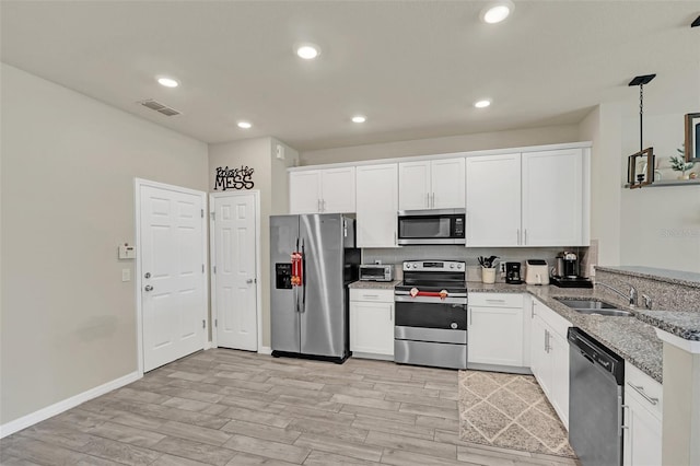 kitchen with light stone counters, stainless steel appliances, sink, decorative light fixtures, and white cabinetry