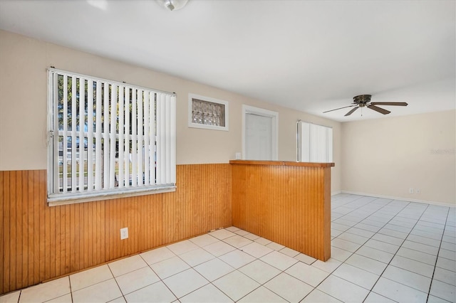 unfurnished room with light tile patterned floors, ceiling fan, and wood walls