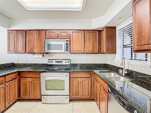 kitchen with light tile patterned floors, stainless steel appliances, dark stone counters, and sink