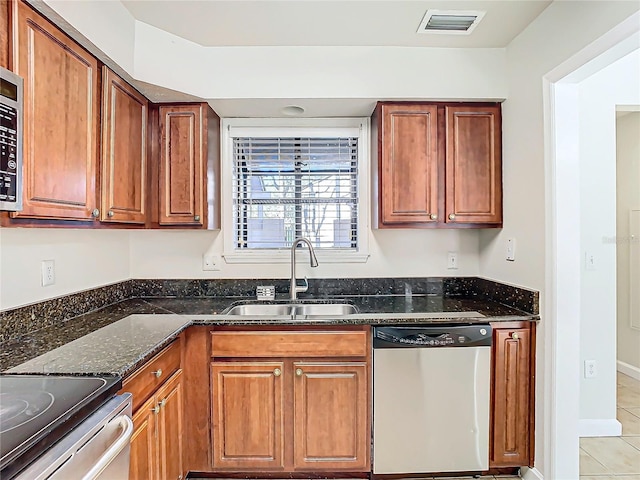 kitchen with dishwasher, light tile patterned floors, sink, and dark stone counters