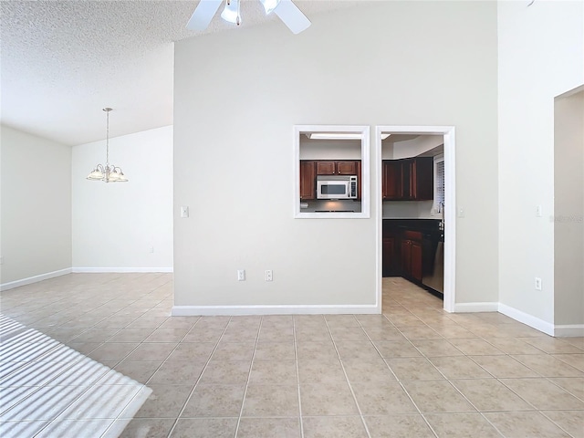 tiled empty room featuring ceiling fan with notable chandelier, a textured ceiling, and high vaulted ceiling