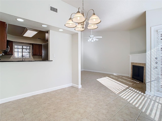 unfurnished living room with ceiling fan with notable chandelier, sink, a tile fireplace, lofted ceiling, and light tile patterned flooring