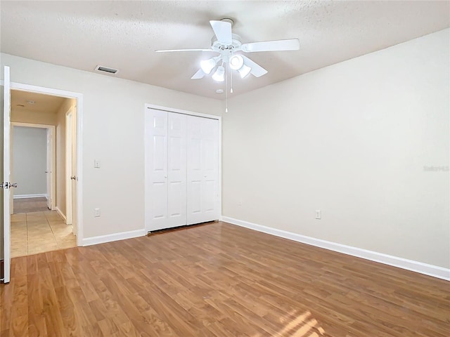 unfurnished bedroom with a closet, ceiling fan, light hardwood / wood-style flooring, and a textured ceiling