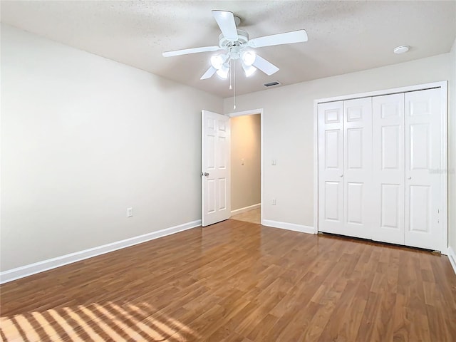 unfurnished bedroom featuring wood-type flooring, a textured ceiling, a closet, and ceiling fan