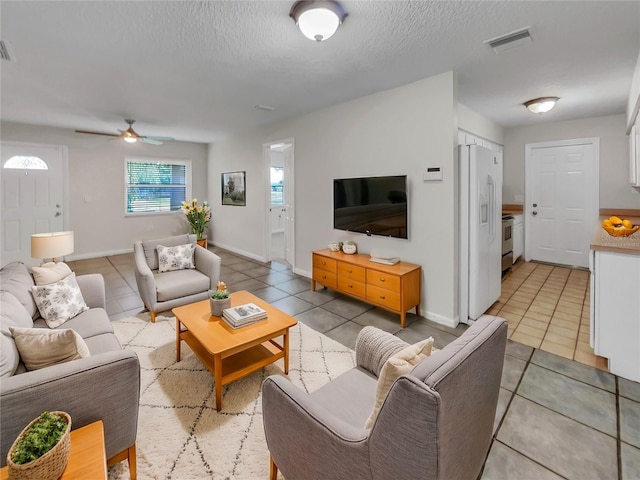 living room with a textured ceiling, ceiling fan, and light tile patterned flooring