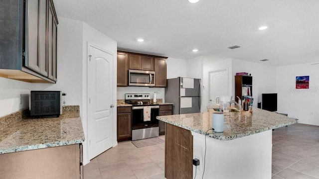 kitchen featuring sink, stainless steel appliances, light stone counters, a kitchen island with sink, and light tile patterned floors