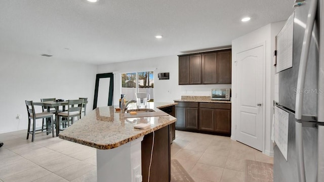 kitchen featuring stainless steel refrigerator, dark brown cabinets, an island with sink, and a textured ceiling