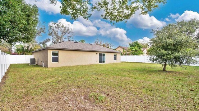 back of property with a yard and central AC