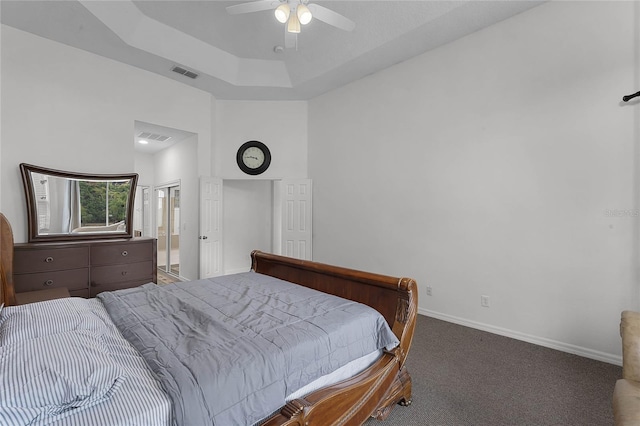 carpeted bedroom featuring a raised ceiling, ensuite bath, ceiling fan, and a high ceiling