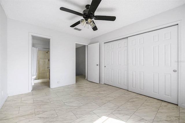 unfurnished bedroom featuring ceiling fan, a closet, a textured ceiling, and ensuite bath