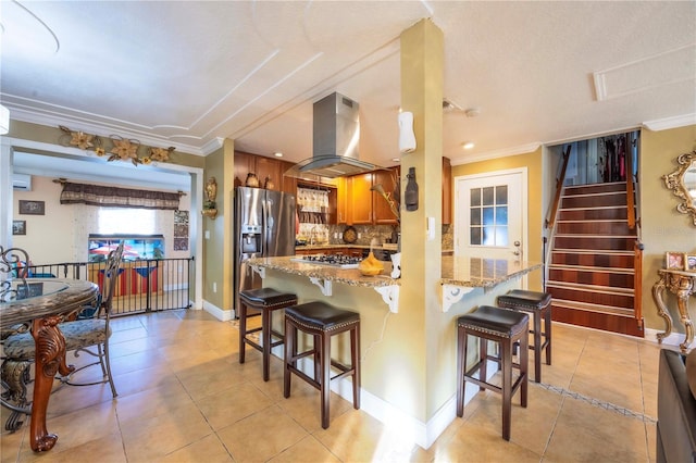 kitchen featuring a kitchen bar, light stone counters, island range hood, appliances with stainless steel finishes, and backsplash