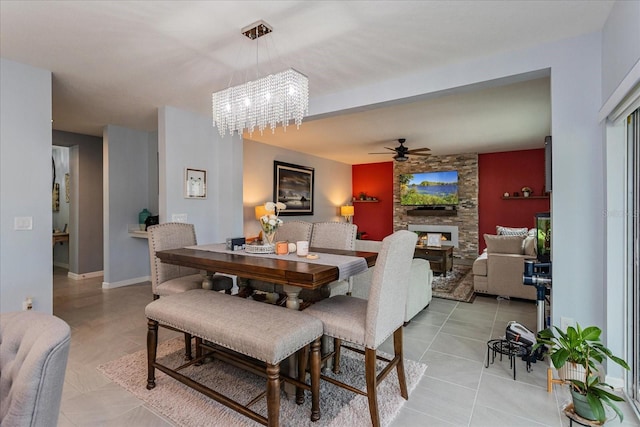 tiled dining room with ceiling fan with notable chandelier and a stone fireplace