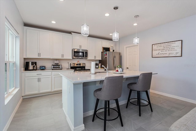 kitchen featuring white cabinets, decorative light fixtures, stainless steel appliances, and an island with sink