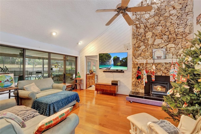 living room featuring a textured ceiling, vaulted ceiling, ceiling fan, hardwood / wood-style floors, and a wood stove