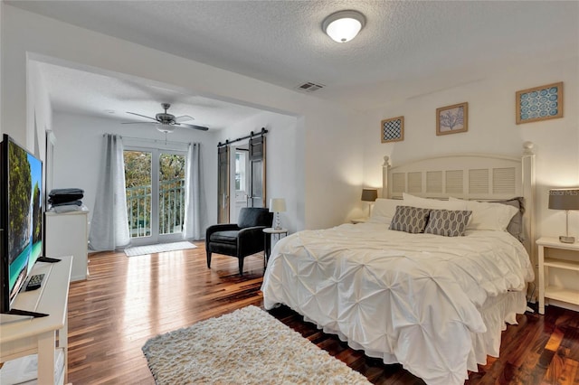 bedroom with access to exterior, a textured ceiling, ceiling fan, wood-type flooring, and a barn door