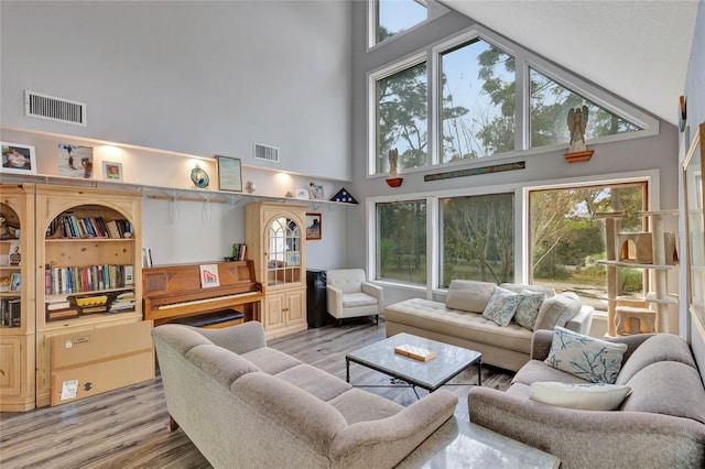 living room with a healthy amount of sunlight, light wood-type flooring, and a towering ceiling